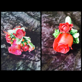 Two red rose boutonnieres with green accents on a dark fabric background