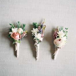 Three small floral boutonnieres with white and pink blooms on a fabric background