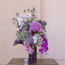 Tall bouquet of pink roses, orchids, and hydrangeas in a glass vase