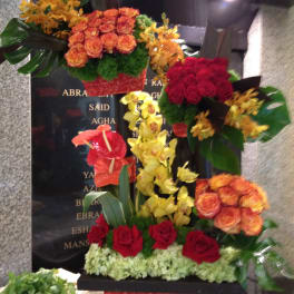 Tall floral tribute with red and orange roses and yellow orchids