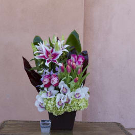Mixed bouquet of lilies, orchids, and roses in a dark vase