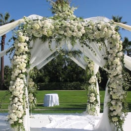 White floral wedding arch draped with fabric outdoors