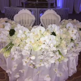 White orchid and rose arrangement on a draped table with two chairs behind it