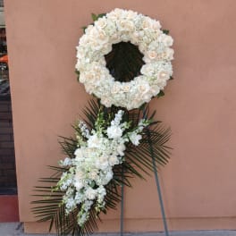 White floral wreath and spray on a stand with palm fronds
