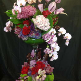 Tall floral arrangement with orchids, roses, and hydrangeas in a glass vase