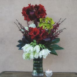 Tall floral arrangement with red, green, and white blooms in a glass vase