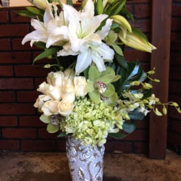 White lilies, cream roses, and green orchids in a silver vase