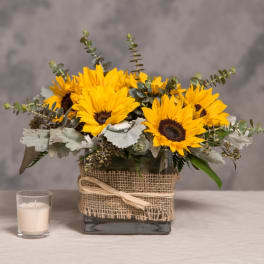 Sunflower arrangement in a square glass vase with burlap wrap and a candle beside it