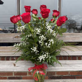 Tall arrangement of red roses with white filler flowers in a clear glass vase with red bow