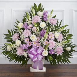 Large pastel floral arrangement in a white vase with a purple ribbon