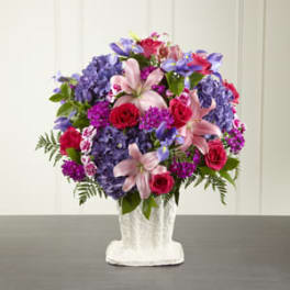 Bouquet of pink lilies, red roses, and purple flowers in a white vase