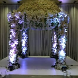 Large white floral wedding arch on a stage with purple lighting