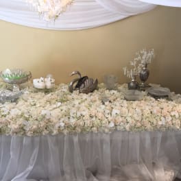 Large table covered in white and blush roses with silver decor pieces
