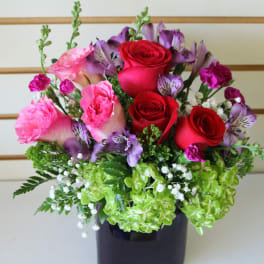 Bouquet of red and pink roses with purple flowers in a dark vase