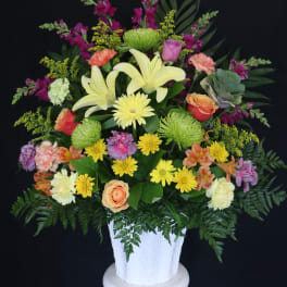 Mixed bouquet in a white pedestal vase with yellow lilies and roses
