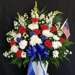 Red, white, and blue floral arrangement in a white vase with an American flag