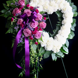Heart-shaped floral wreath with white carnations and pink roses on a black stand