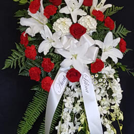 Red roses and white lilies arranged with a white ribbon on a black stand