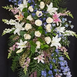 Standing funeral spray with white lilies, roses, and blue flowers