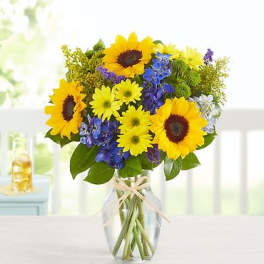Sunflowers and blue flowers in a clear glass vase with a ribbon