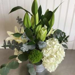Arrangement of white hydrangea and lilies with green buds in a metal vase