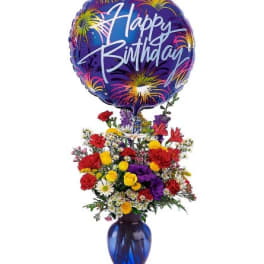 Colorful mixed flower arrangement in a blue vase with a large Happy Birthday balloon on top.