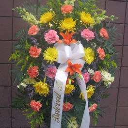 Standing funeral wreath with yellow and coral flowers and a white ribbon
