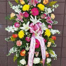 Tall standing spray of mixed flowers with pink ribbons on an easel
