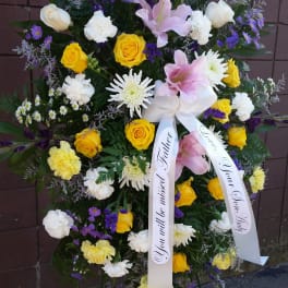 Standing sympathy spray with yellow and white roses, lilies, and purple flowers