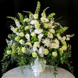 White and pale green floral arrangement in a white vase with ribbon