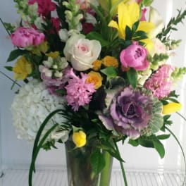 Tall mixed bouquet in a clear glass vase with pink, yellow, white, and purple flowers