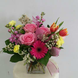 Mixed bouquet of pink roses, gerbera daisies, and tulips in a glass vase