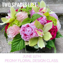 Low arrangement of pink peonies, roses, green hydrangea and orchids in a round glass vase on stone steps.