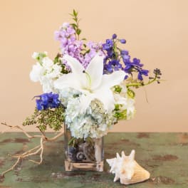 White lily bouquet with blue and lavender flowers in a glass vase