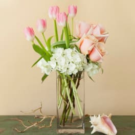 Pink tulips and blush roses in a clear glass vase with white hydrangeas