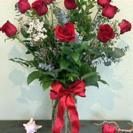 Tall bouquet of red roses in a glass vase with a red ribbon