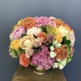 Large mixed bouquet in a gold vase with pink, peach, yellow, and white blooms