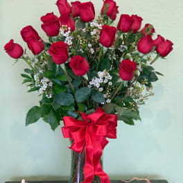 Red roses arranged in a glass vase with a red ribbon bow