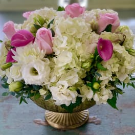 Pink roses and white hydrangeas arranged in a gold pedestal bowl