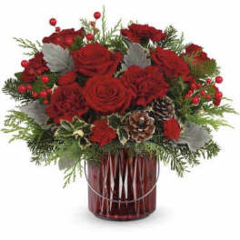 Red roses arranged in a red glass vase with pinecones and greenery