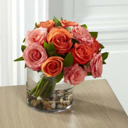 Pink and orange roses in a clear glass vase with pebbles