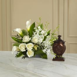 White floral arrangement with calla lilies and roses beside a dark urn