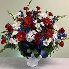 Patriotic red, white and blue flower arrangement in a white urn with a navy bow.