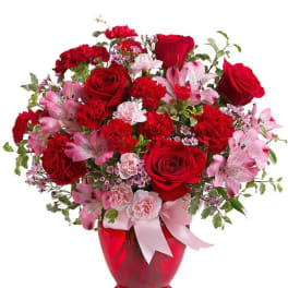 Red roses and pink flowers arranged in a red vase with a pink ribbon