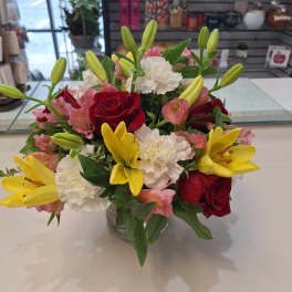 Bouquet of red roses, yellow lilies, and white carnations in a glass vase