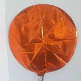 Orange round foil balloon against a white wall