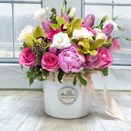 Pink and white flowers arranged in a white hat box with a ribbon