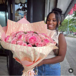 Woman holding a large bouquet of pink roses wrapped in patterned paper