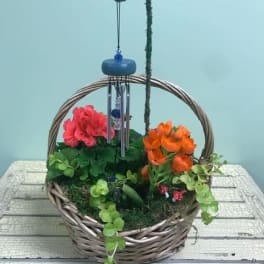Basket arrangement with pink and orange flowers and a hanging wind chime