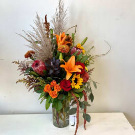 Tall mixed bouquet with orange lilies, red roses, and sunflowers in a glass vase